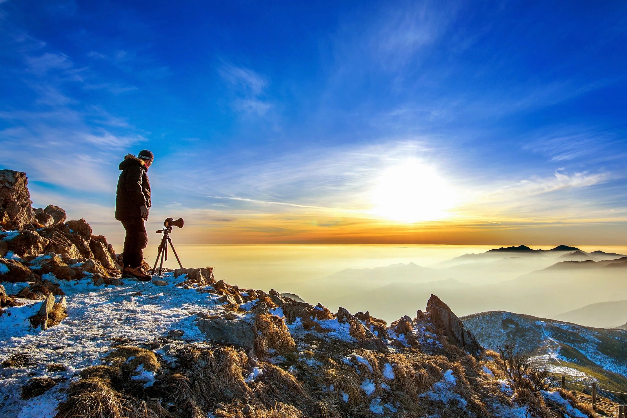 View from the mountains observing the sunset in colours of white, yellow, and gold with a vast blue sky.
